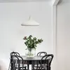 A white pendant lamp hangs above a round black dining table with a vase of flowers and chairs. Produktbild-Vorschau