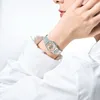 A close-up shot of a person's wrist wearing a silver digital watch with a pink face. Produktbild-Vorschau