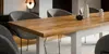 A close-up shot of a wooden dining table with white legs, set in a modern dining room with grey chairs. Produktbild-Vorschau