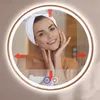 A woman with a towel on her head is touching her face in front of a lighted mirror. Produktbild-Vorschau