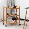A wooden serving cart with three shelves, filled with various items, is shown in a room setting. Podgląd zdjęcia produktu