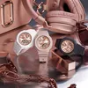 A collection of rose gold and pastel-colored accessories, including three watches, headphones, a handbag, and sunglasses, arranged on a metallic surface. Anteprima dell’immagine prodotto