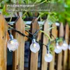 String lights with clear, bulb-shaped lights are strung along a wooden fence. Anteprima dell’immagine prodotto