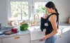 A woman is holding a baby in a carrier in a kitchen. Náhled obrázku produktu