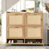 A wooden shoe cabinet with rattan doors is shown in a hallway setting, next to a staircase with white paneling. Náhľad obrázku produktu