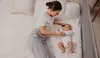 A woman is lying on a bed next to a baby, with a bed rail visible on the side. Voir les images du produit