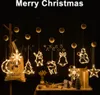 Christmas-themed window lights with various shapes like a star, moon, Christmas tree, reindeer, bell, snowman, and snowflake, hanging against a dark background. A bag with text is visible behind some of the lights. A table with decorative items is in the f Produktbild-Vorschau