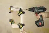 A person is using a cordless drill to screw pieces of wood together, which are held in place by corner clamps. Produktbild-Vorschau