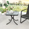 A small square glass-top table with a black metal base is placed on a patio next to a black chair. Several potted plants are visible in the background. Podgląd zdjęcia produktu