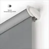 Close-up of a gray roller blind with a white mounting bracket attached to a white wall. A small icon and text indicating 'Starker Verdunklungs-Effekt' (strong blackout effect) are in the upper left corner. Anteprima dell’immagine prodotto