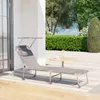 A gray chaise lounge chair with a small attached table sits on a wooden deck next to a white wall, with a lush green garden in the background. Produktbild-Vorschau