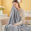 A woman is sitting on a couch, holding a gray blanket. Produktbild-Vorschau