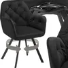 A black velvet armchair with tufted detailing is shown from the front, with a circular arrow graphic indicating rotation around its base. Another armchair is partially visible in the foreground. Produktbild-Vorschau