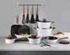 A collection of white cookware with wooden handles is displayed on a countertop against a light gray wall. Produktbild-Vorschau