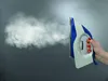 A hand holding a steam iron that is emitting a large cloud of steam. Náhled obrázku produktu