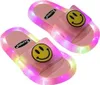 Paar pinke leuchtende Rutsche-Sandalen mit gelben Smiley-Aufklebern auf den Riemen
