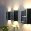 Three solar-powered wall lights mounted on a wall, with light beams illuminating upwards and downwards. A plant is in the foreground. Náhľad obrázku produktu