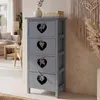 A grey-blue chest of drawers with heart cutouts is shown in a room with a sofa and a macrame wall hanging.