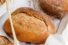 Two loaves of artisan bread in a basket, one in the foreground and another slightly out of focus in the background. Produktbild-Vorschau