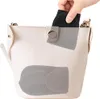 A hand is placing a black accessory into a white handbag. Náhled obrázku produktu