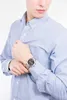 A person wearing a light blue button-down shirt and a silver and black watch on their left wrist. Náhled obrázku produktu