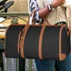 A person holding a black duffel bag with brown leather accents. Produktbild-Vorschau