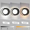 A collage of three images showing a modern black and white ring-shaped lamp with different light color temperatures: cool white, natural white, and warm white. Below the images are labels for each light color and a color temperature slider. Náhled obrázku produktu