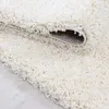 A close-up view of a fluffy, cream-colored shaggy rug, with a portion of it folded over to reveal the backing. Anteprima dell’immagine prodotto