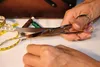 Hands using scissors to cut thread, with sewing supplies in the background. Náhled obrázku produktu