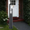A modern outdoor lamp post with three illuminated columns stands on a paved path in front of a brick house with a white door. Produktbild-Vorschau