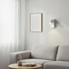A modern living room scene with a sofa, a coffee table with a mug and books, a framed picture on the wall, and a wall lamp. Podgląd zdjęcia produktu