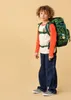 A young boy wearing a backpack stands against a plain background. Produktbild-Vorschau