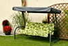 A garden swing with a green and white floral cushion and a gray canopy, set on a green lawn next to a wall and a wooden lattice fence. Produktbild-Vorschau