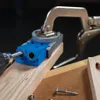 A close-up shot of a Kreg pocket-hole jig being used to drill a hole in a piece of wood, held in place by a clamp. Screws are visible in the foreground. Voir les images du produit