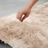Nahaufnahme einer Hand, die einen weichen, zotteligen beigen Teppich auf hellgrauem Boden berührt Anteprima dell’immagine prodotto