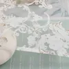 A close-up of a decorative lace trim with a floral pattern, layered over a light blue and tan background with text. Produktbild-Vorschau