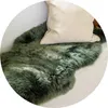A close-up view of a green sheepskin rug with a beige pillow on top. Produktbild-Vorschau