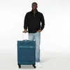 A man stands next to a teal suitcase against a white background. Podgląd zdjęcia produktu