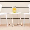 A white metal side table with a pitcher of lemonade and a glass on it, placed between two white chairs against a light-colored wall with black stripes. Voir les images du produit