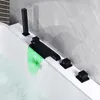 A close-up view of a modern bathtub faucet with a waterfall spout and LED lighting, filling a bathtub with water. Produktbild-Vorschau