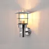 A modern outdoor wall lamp with a motion sensor is mounted on a light gray wall, illuminated by its own light. Produktbild-Vorschau
