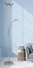 A modern floor lamp with a reading light, placed in a room with a blue wall and a sofa in the background. Produktbild-Vorschau