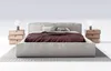 A modern bed with a headboard, duvet, pillows, and two nightstands with lamps on either side, set against a white background. Náhled obrázku produktu