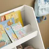 A close-up view of a white bookshelf filled with children's books and a light blue backpack hanging on the wall. Náhľad obrázku produktu
