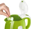 A hand is shown inserting a filter into a green electric kettle. Podgląd zdjęcia produktu