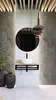 A modern bathroom vanity with a black metal console shelf holding a white vessel sink, mounted on a tiled wall with a round mirror above. Decorative vases and a plant are placed on the floor. Anteprima dell’immagine prodotto