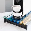 A white coffee machine sits on a glass and metal stand that holds coffee capsules. Podgląd zdjęcia produktu