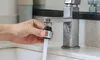 A hand is holding a faucet extender under a running faucet. Produktbild-Vorschau