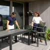 A couple is setting up an outdoor dining area on a wooden deck, arranging chairs around a table. Náhled obrázku produktu