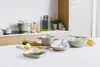 A collection of cookware and kitchen utensils arranged on a white countertop in a modern kitchen setting. Produktbild-Vorschau
